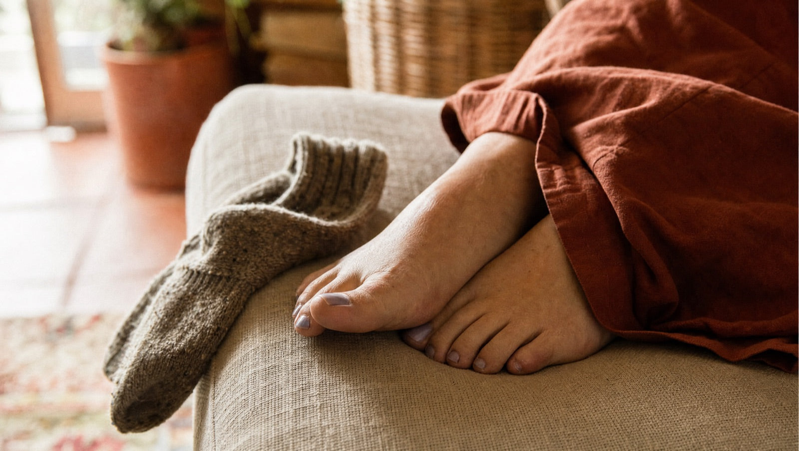 Bare feet with faintly cold, blue-tinged toenails on a couch in a warm room, thick wool socks kicked off beside them