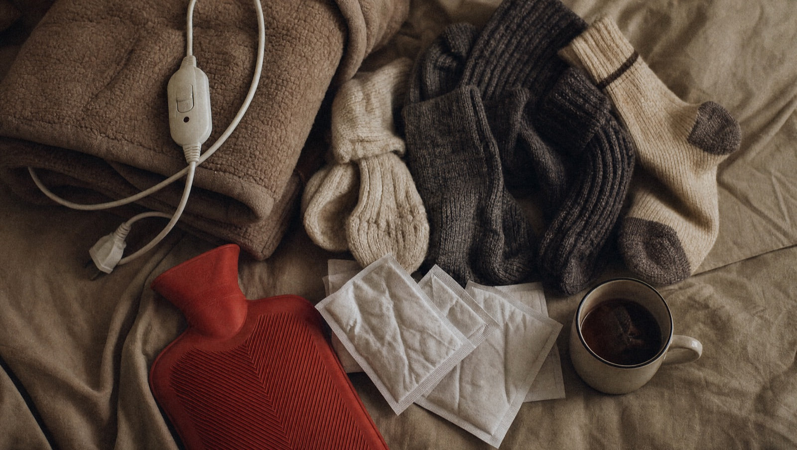 A pile of external warming fixes that never worked — a heated blanket, hand warmers, thick socks and a hot water bottle