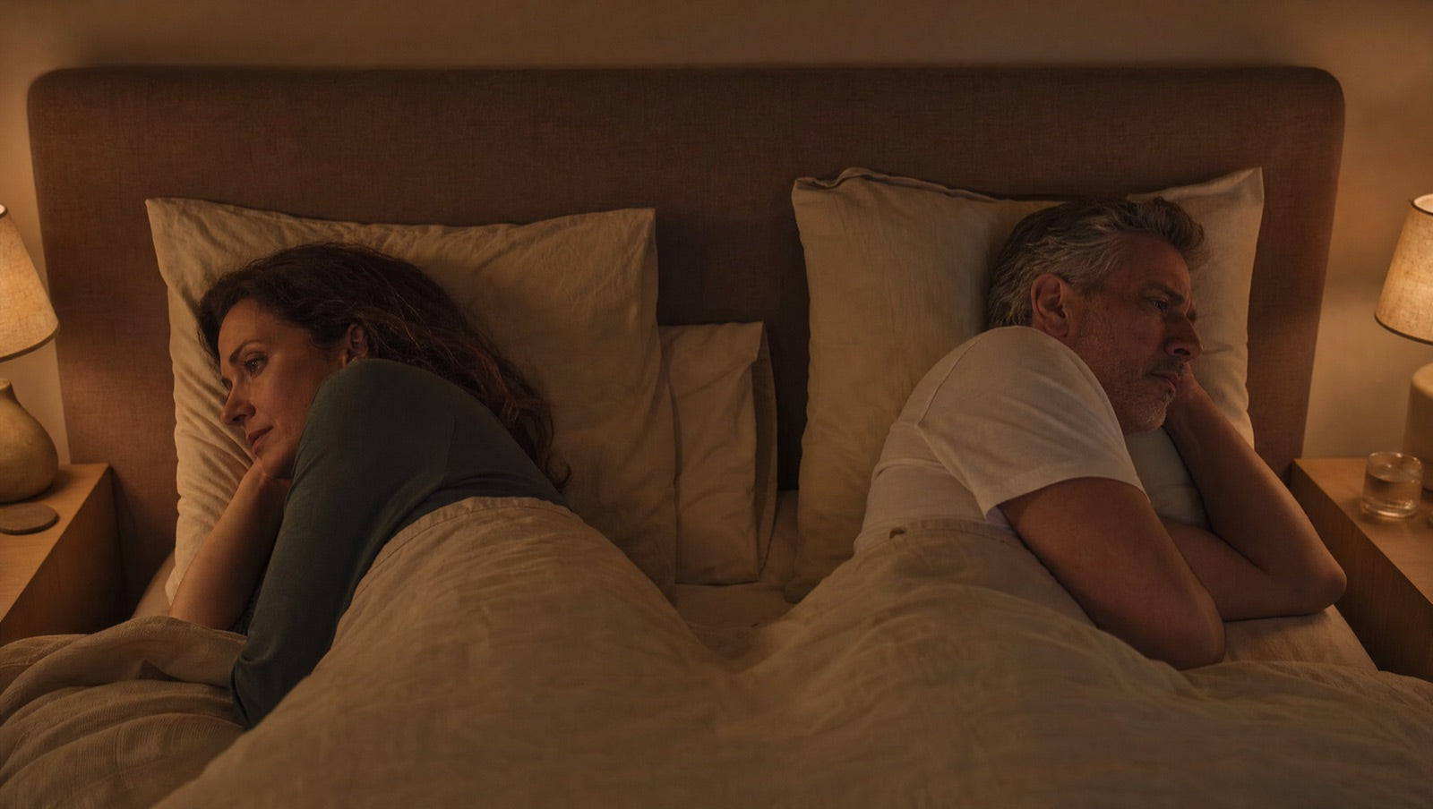 A couple lying awake in bed at night with a quiet distance between them