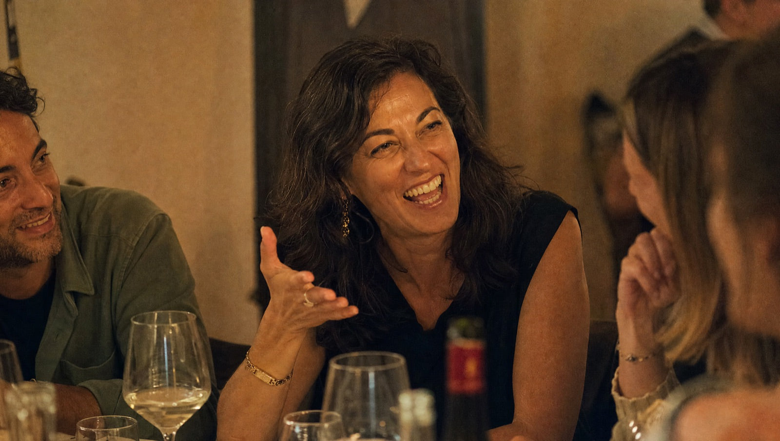 A woman sharp and present again, laughing mid-conversation at a dinner with friends