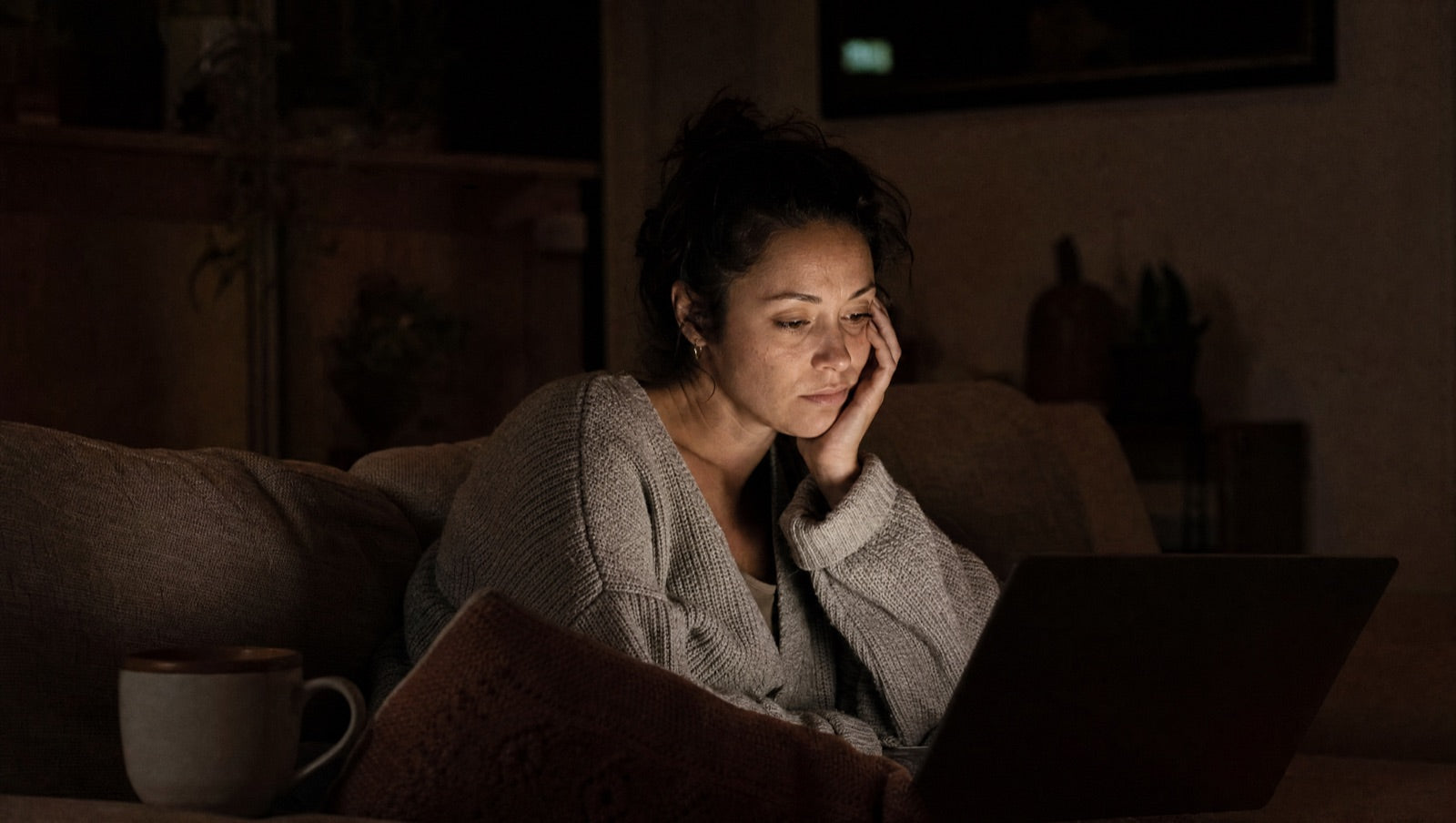 A woman reading online forums and other women's stories late at night by laptop glow
