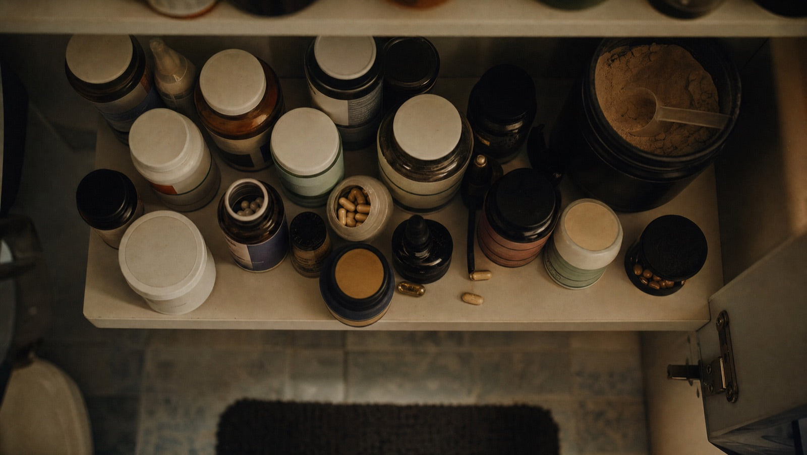 A cabinet shelf crowded with single-symptom fixes bought separately: sleep aid, focus pills, diet powder and vitamins